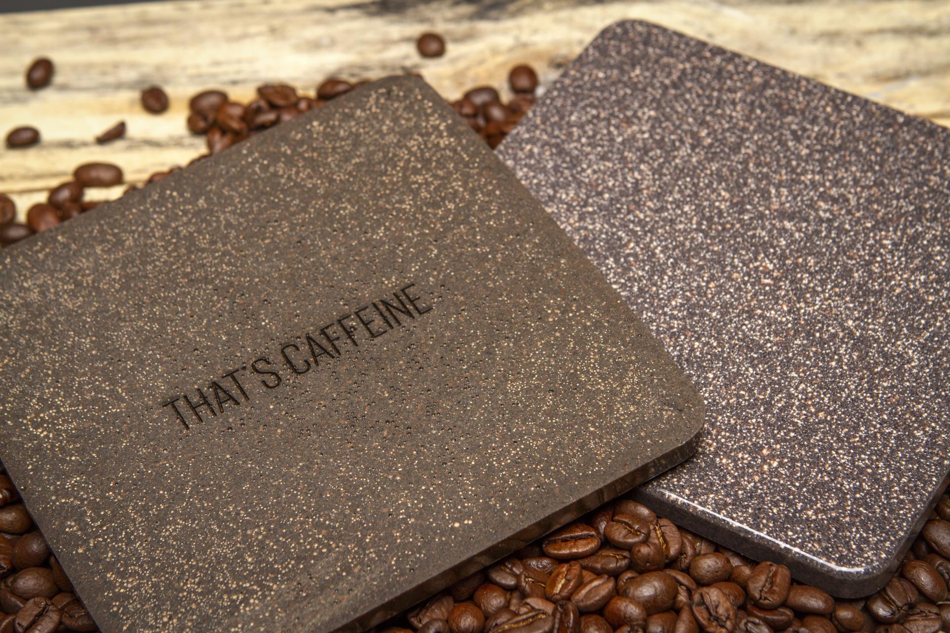 Lightweight granite-like coasters labeled "That's Caffeine," surrounded by coffee beans, showcasing sustainable design.