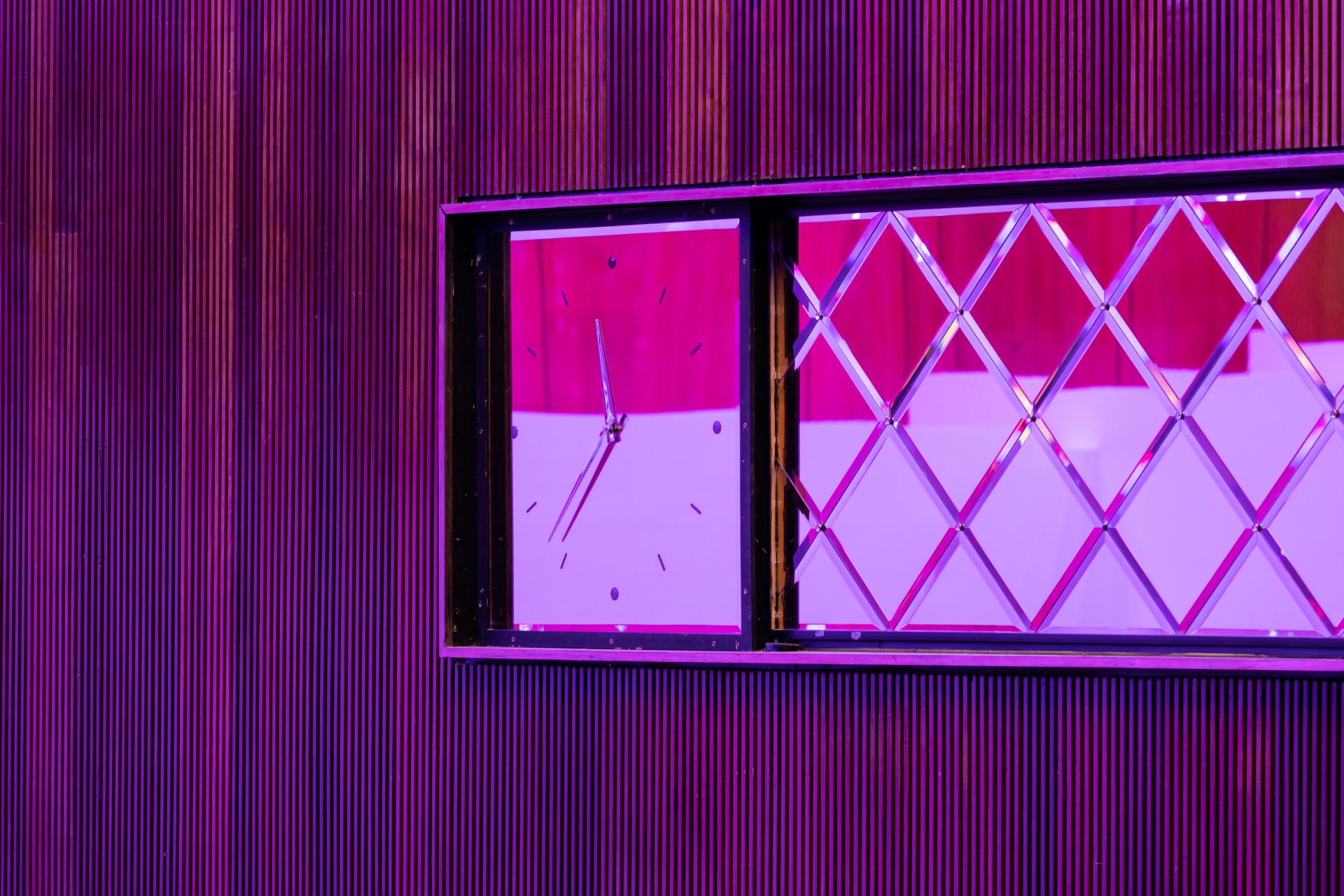 Bold clock with diamond-patterned window against a textured purple wall, reflecting the vibrant atmosphere of New Century venue.