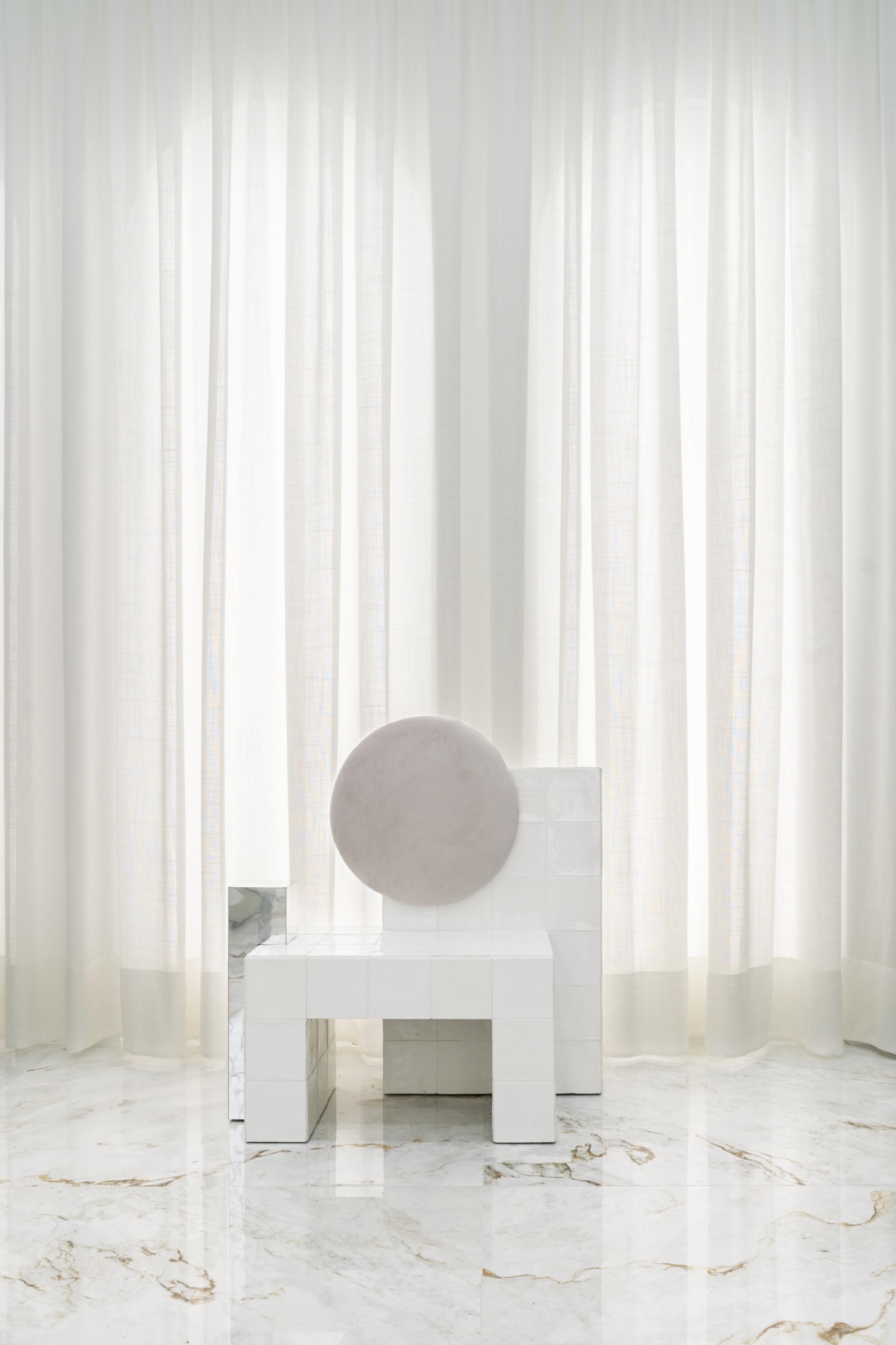 Ceramic chair design featuring a round cushion, set against sheer curtains in a contemporary interior space.