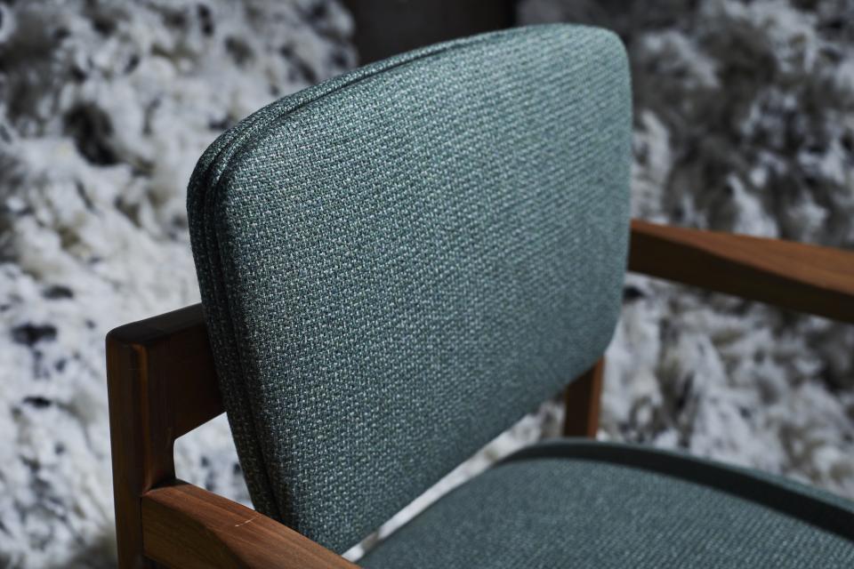 Tweed upholstery on a wooden chair showcases Camira's Main Line Twist textile in a rich, textured green hue.