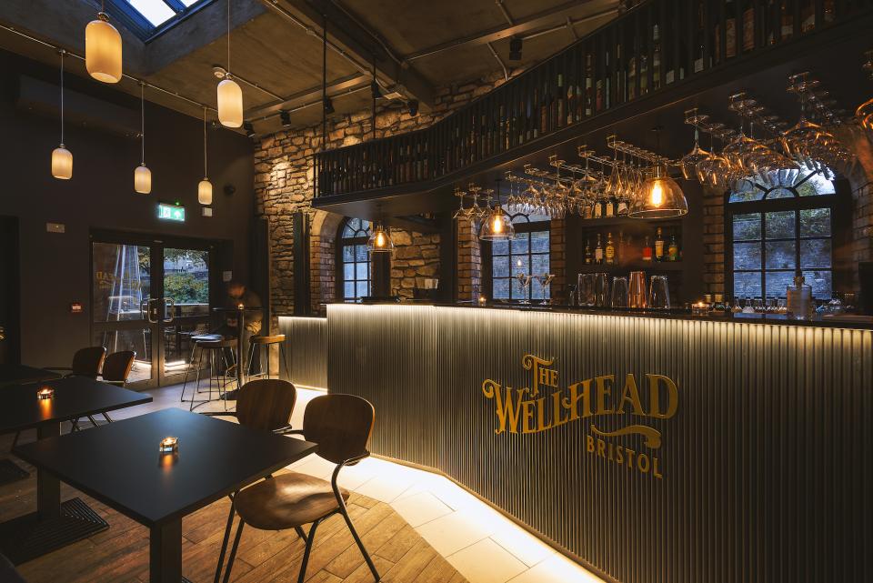 Stylish interior of The Wellhead in Bristol featuring illuminated bar, wooden decor, and cozy seating arrangements.