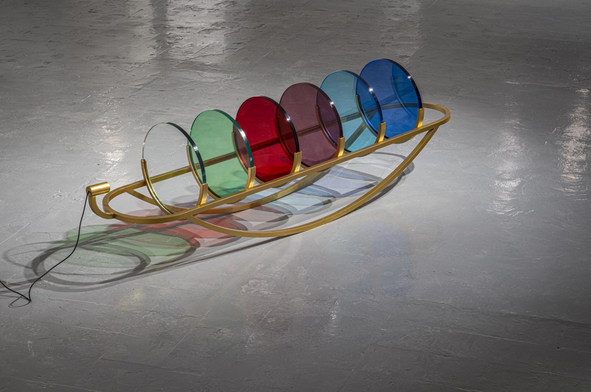 Colorful glass disks arranged on a gold frame, showcasing innovative design at the GLASS to GLASS exhibit in Venice.