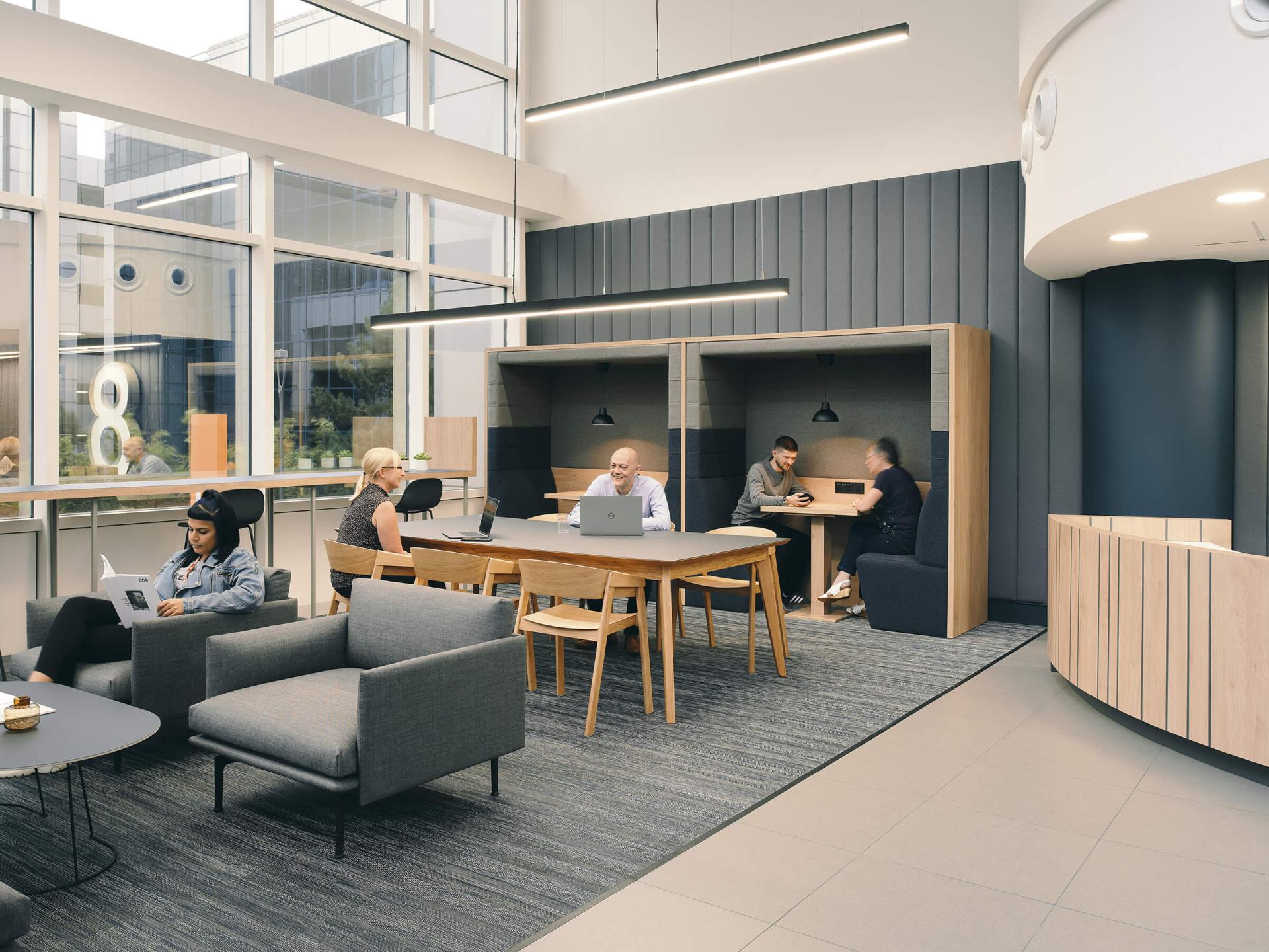 Modern office interior showcasing collaborative spaces with people engaging in sustainable design discussions and creative work.