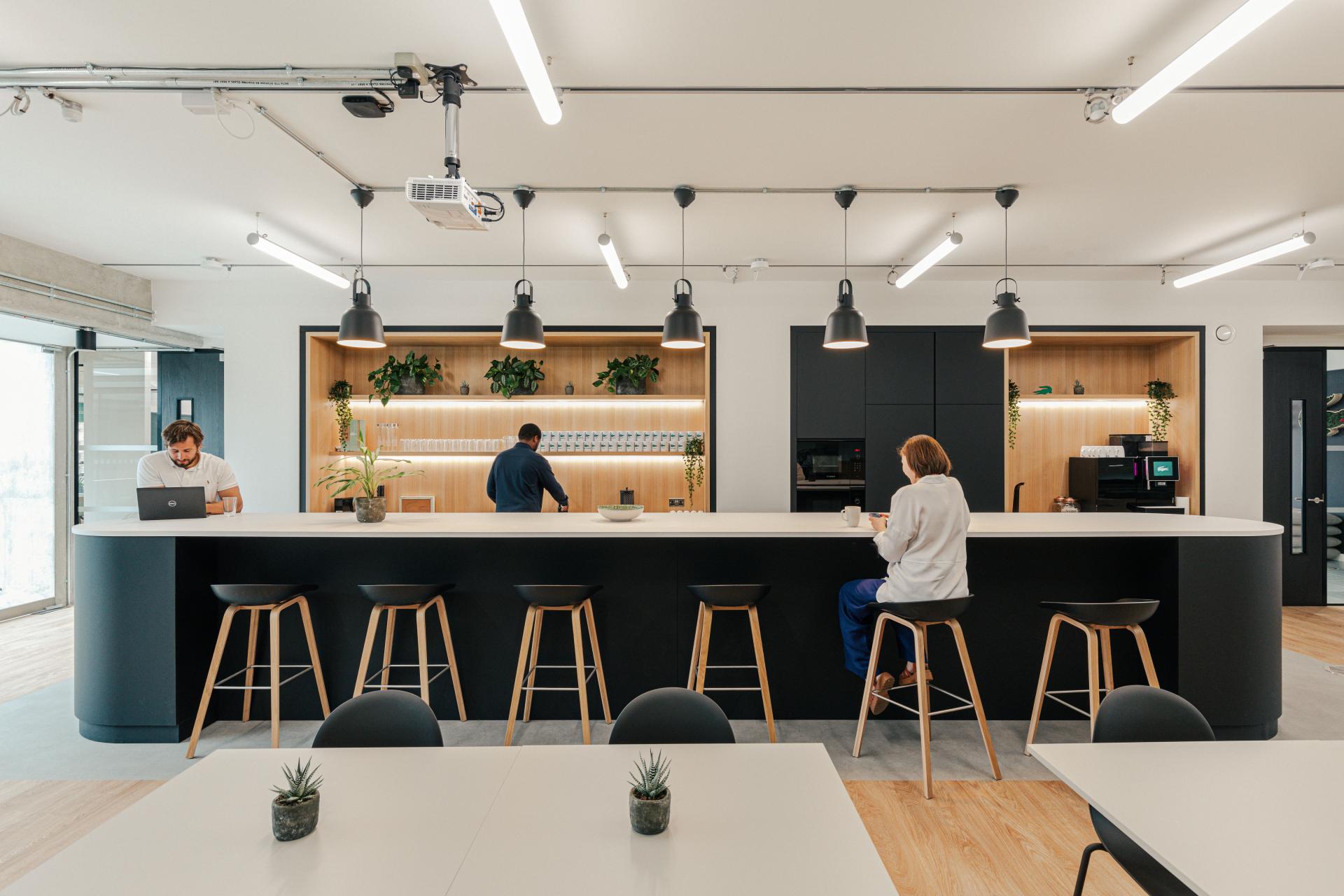 Modern workspace kitchen designed for Lacoste, featuring sleek furniture and plants, capturing a New York warehouse aesthetic.