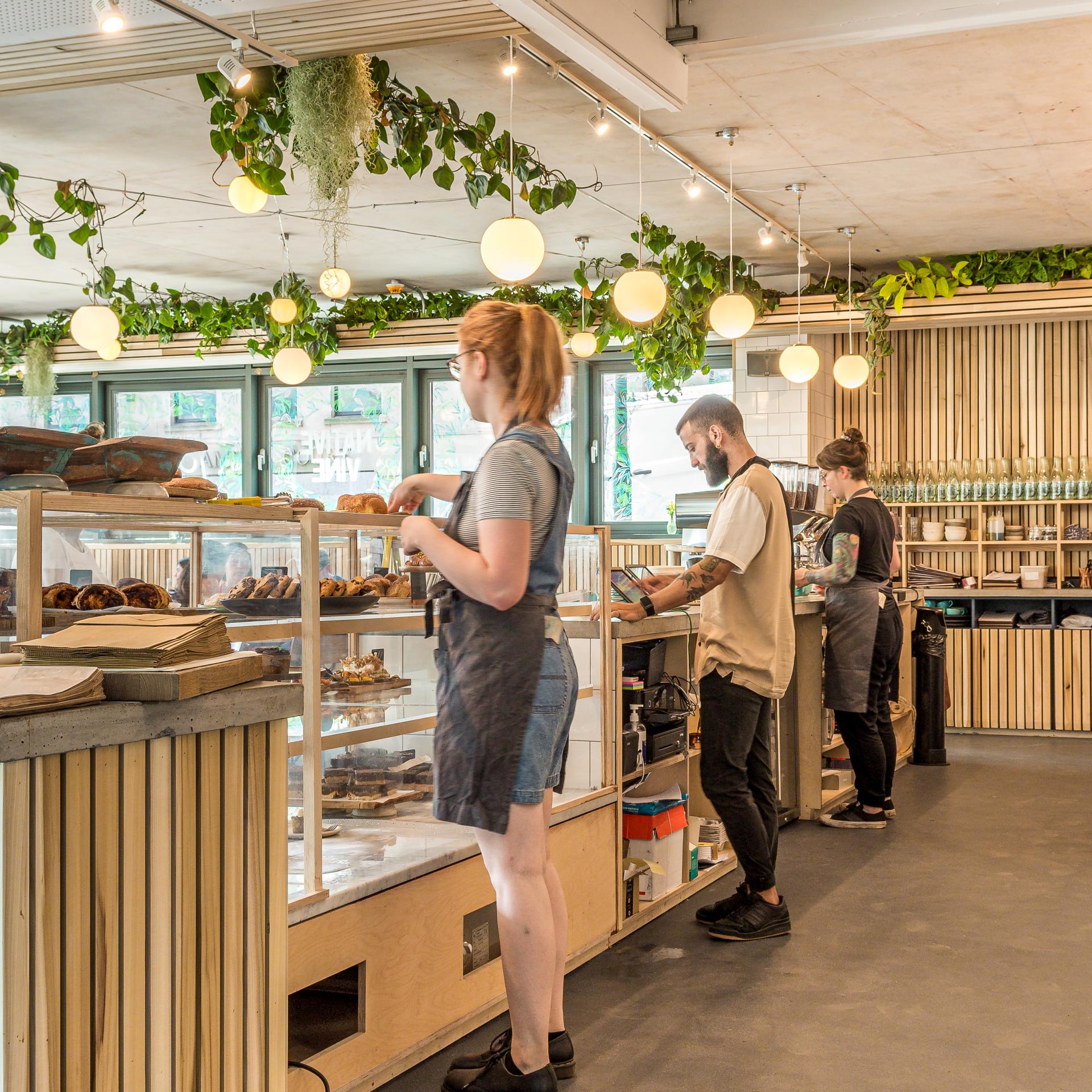 Bristol Loaf café staff serving customers with freshly baked goods in a modern, plant-filled bakery setting.
