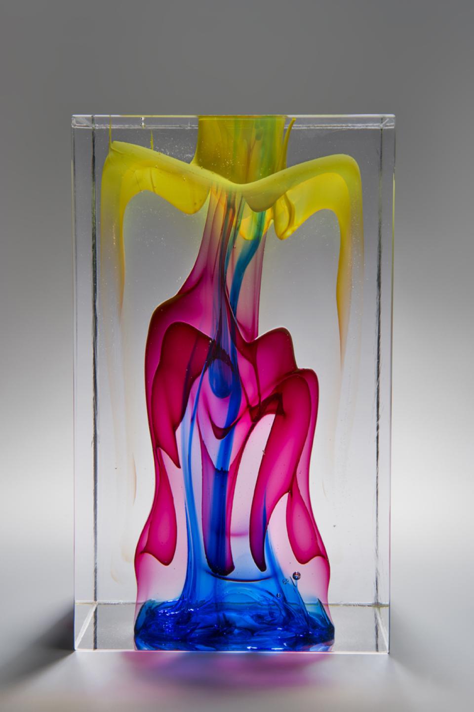 Colorful glass sculpture by Tim Rawlinson featuring vibrant yellow, pink, and blue swirls on display at London Glassblowing.