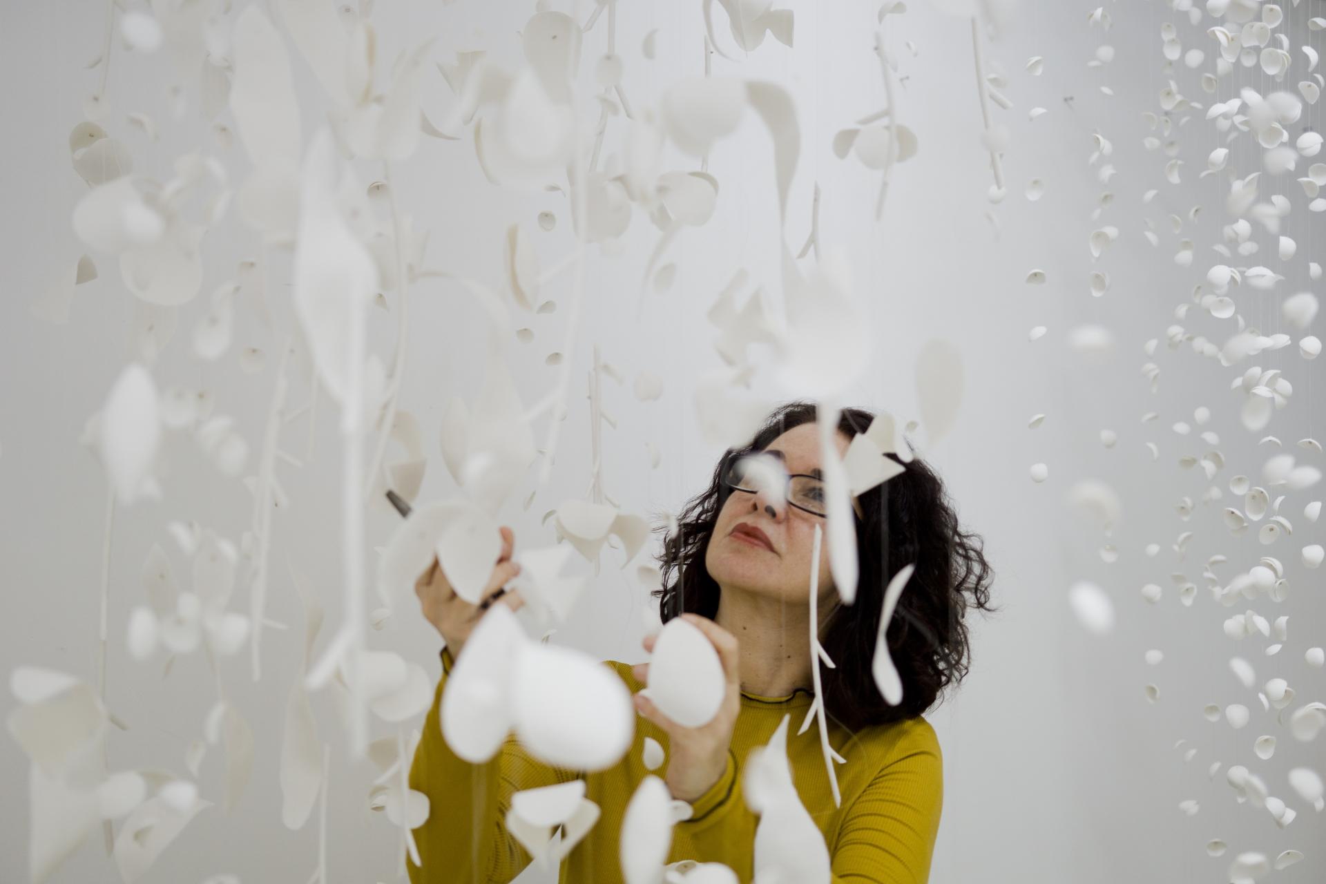 An artist interacts with delicate white paper motifs, creating a mesmerizing installation for London Craft Week 2019.