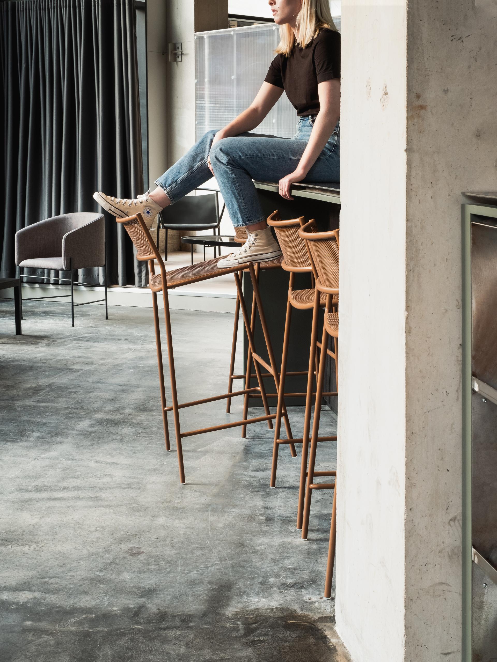 A young woman in casual attire poses on a bar counter amidst modern interior design elements in Manchester.