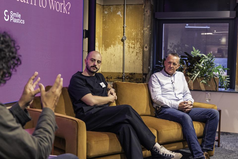 Two speakers engaged in discussion on technology's role in the modern workplace, with a backdrop displaying a relevant question.