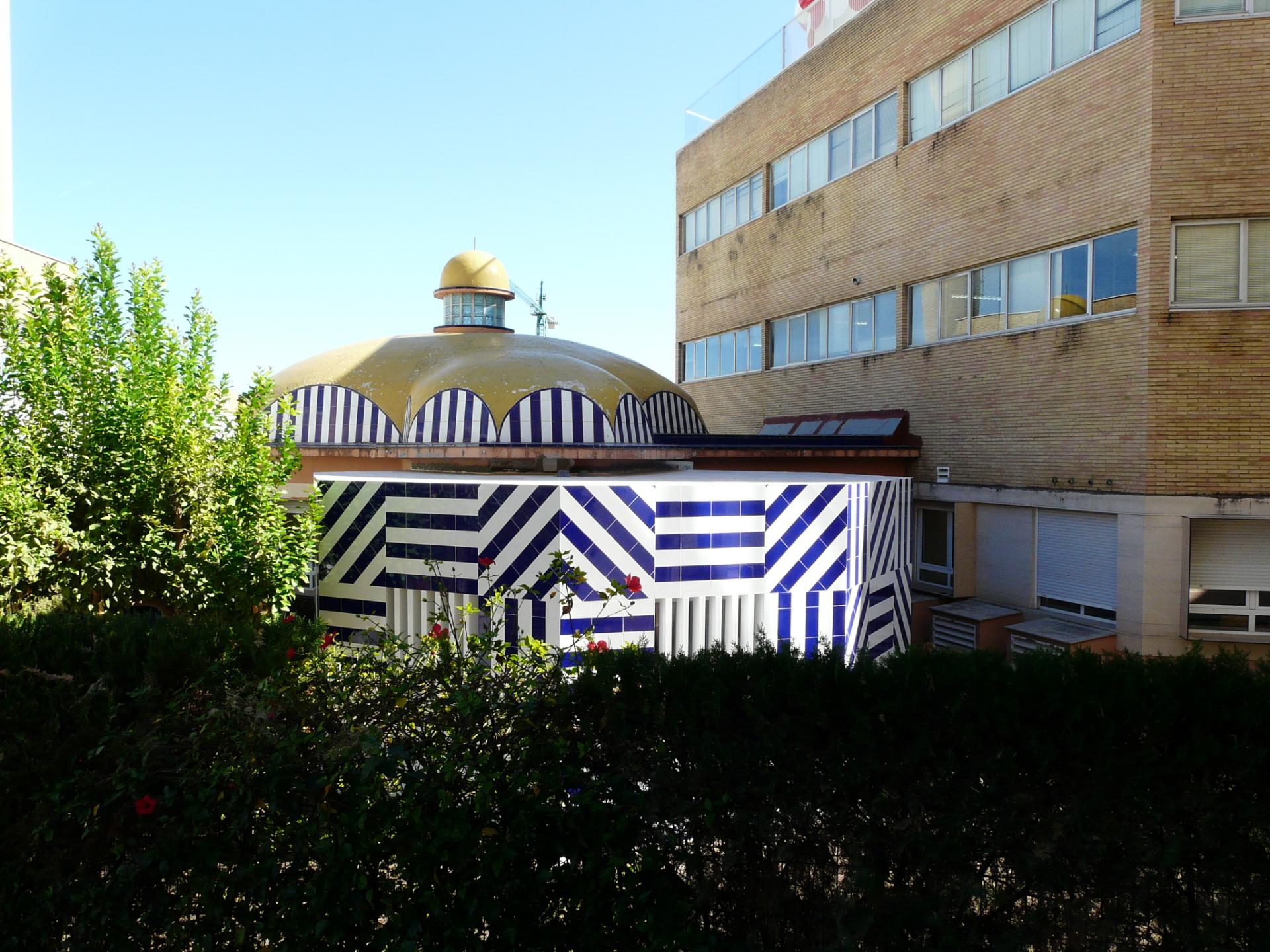 Colorful ceramic-clad building featuring distinctive dome, surrounded by greenery, showcasing innovative Spanish interior design.