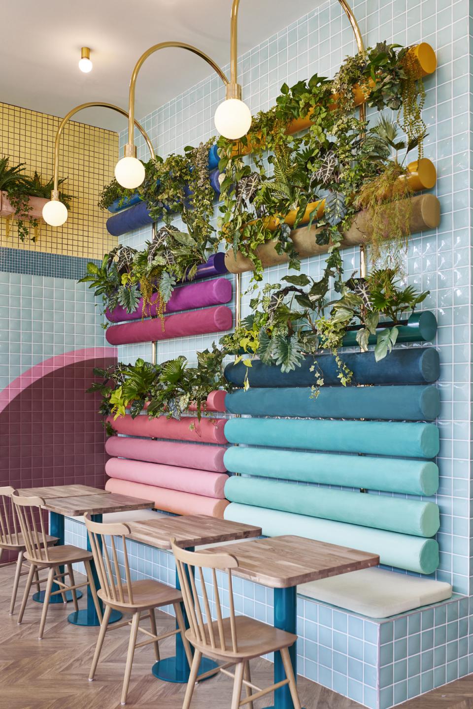 Contemporary seating area with colorful cushioned benches and greenery, designed by Masquespacio for Piada restaurant in Lyon.