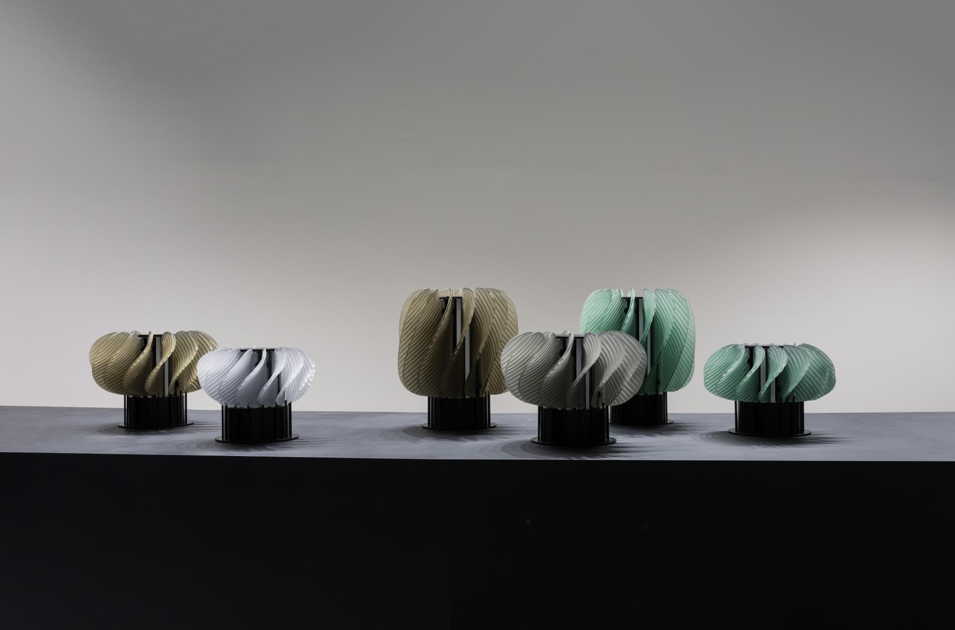 Elegant sculptural lighting installations in various colors displayed on a dark surface at WonderGlass's London showroom.