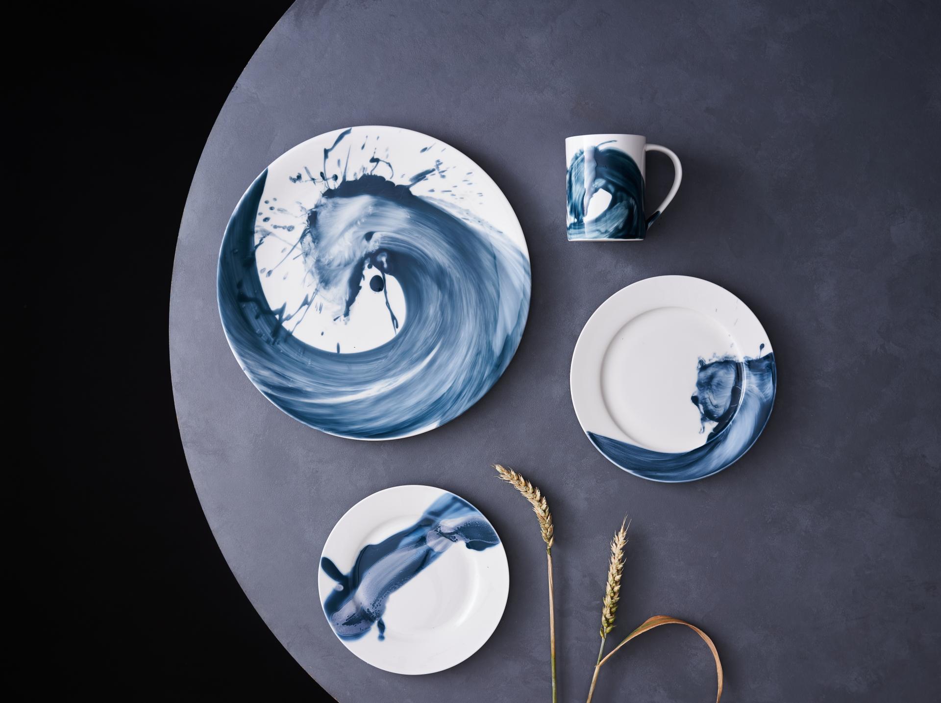 Ceramic plates and mug featuring blue wave patterns by designer Reiko Kaneko, arranged on a dark surface.