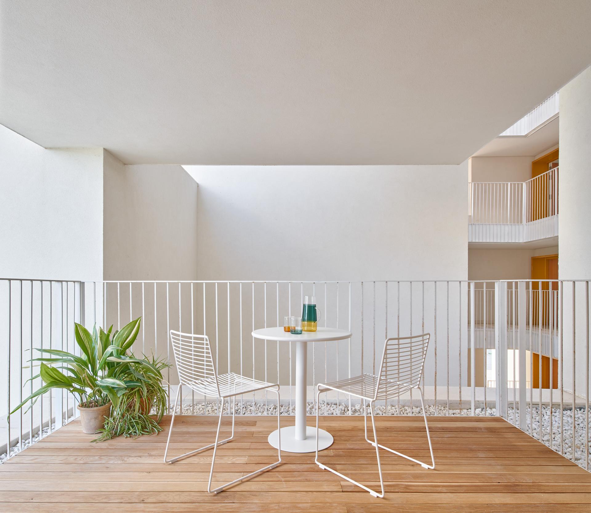 Modern balcony featuring white chairs and a table, showcasing innovative tile designs in contemporary Spanish architecture.