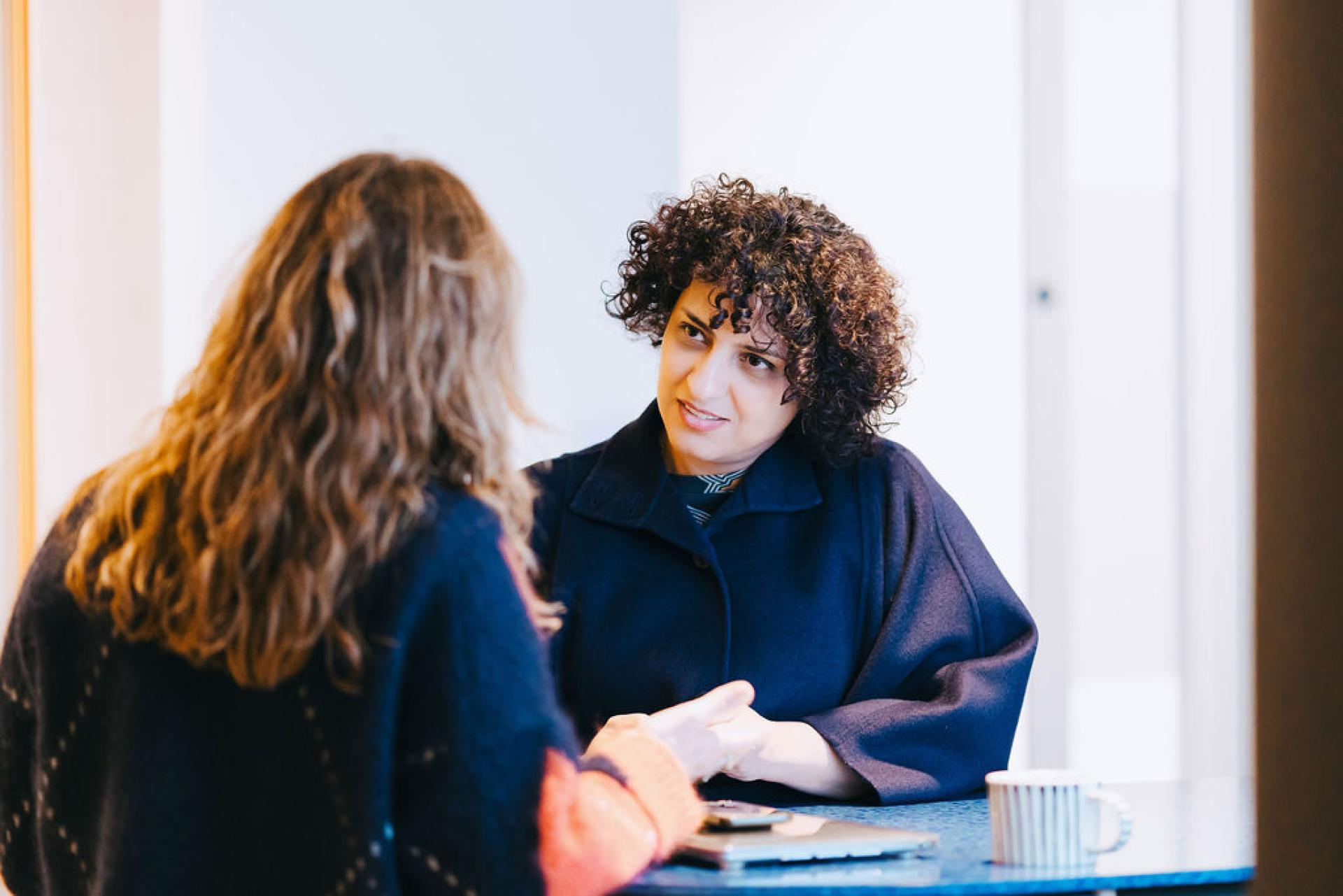 Two women engaged in a conversation, discussing sustainable solutions at a bright and modern workspace setting.