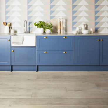 Stylish kitchen featuring blue cabinetry, a farmhouse sink, and light wood flooring from Domus' new Pergo flooring collection.