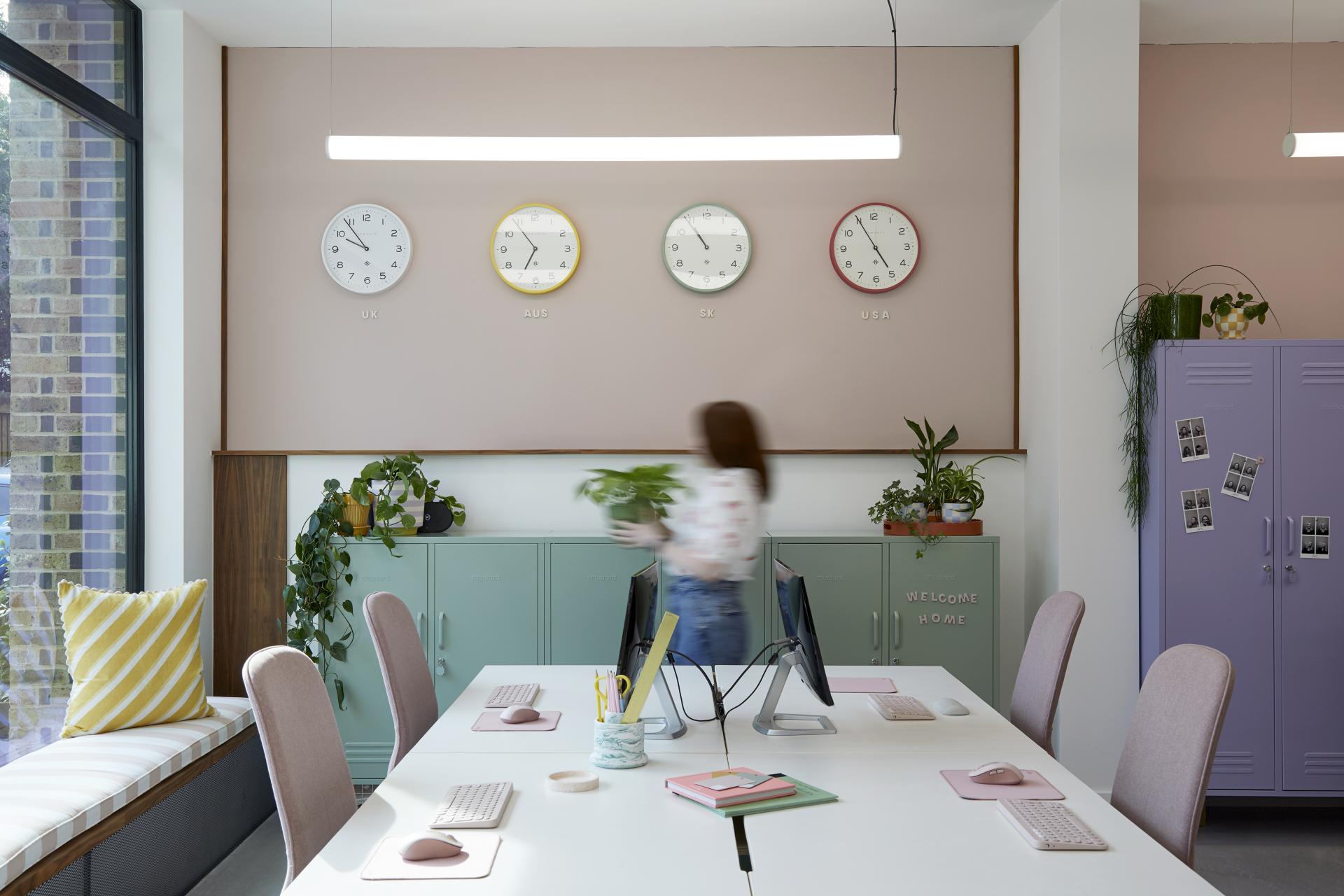 Bright and colorful Mustard Made office featuring plants, workstations, and clocks displaying different time zones.