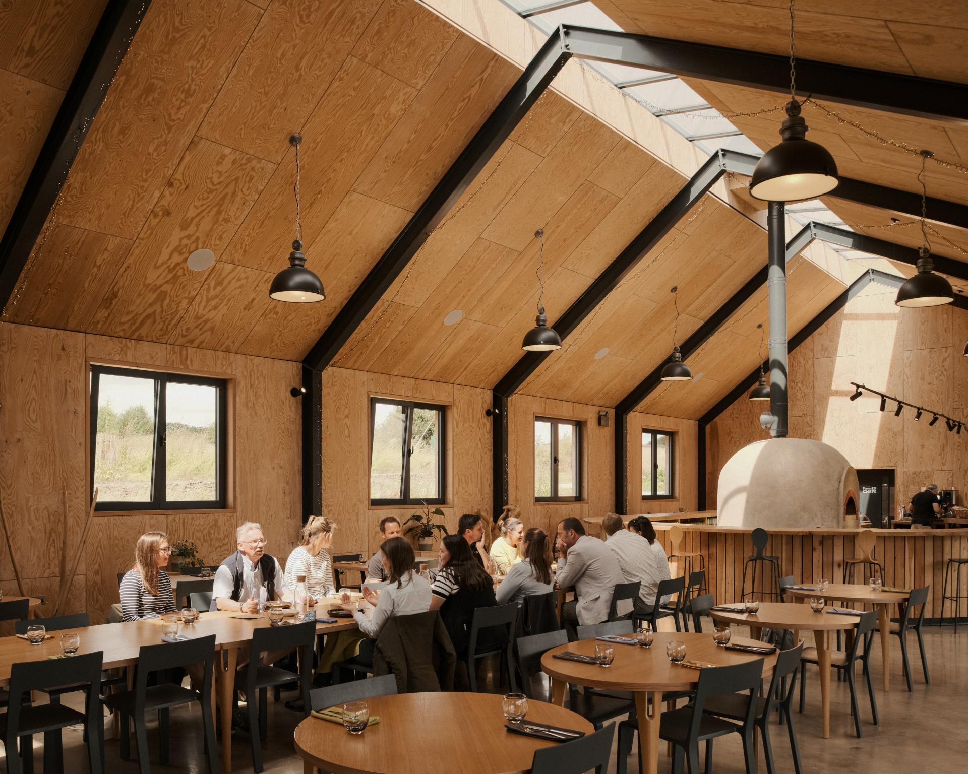 Modern sustainable dining area inside the FarmED education centre, featuring wooden beams, natural light, and visitors enjoying a meal.