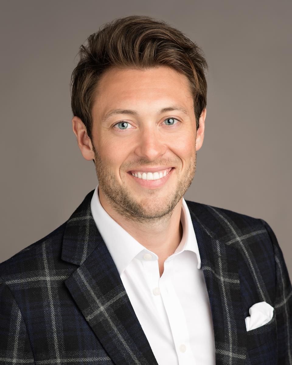 Rollie Attard, COO of Panaz, smiles confidently in a stylish plaid blazer, representing heritage and innovation in the hospitality industry.