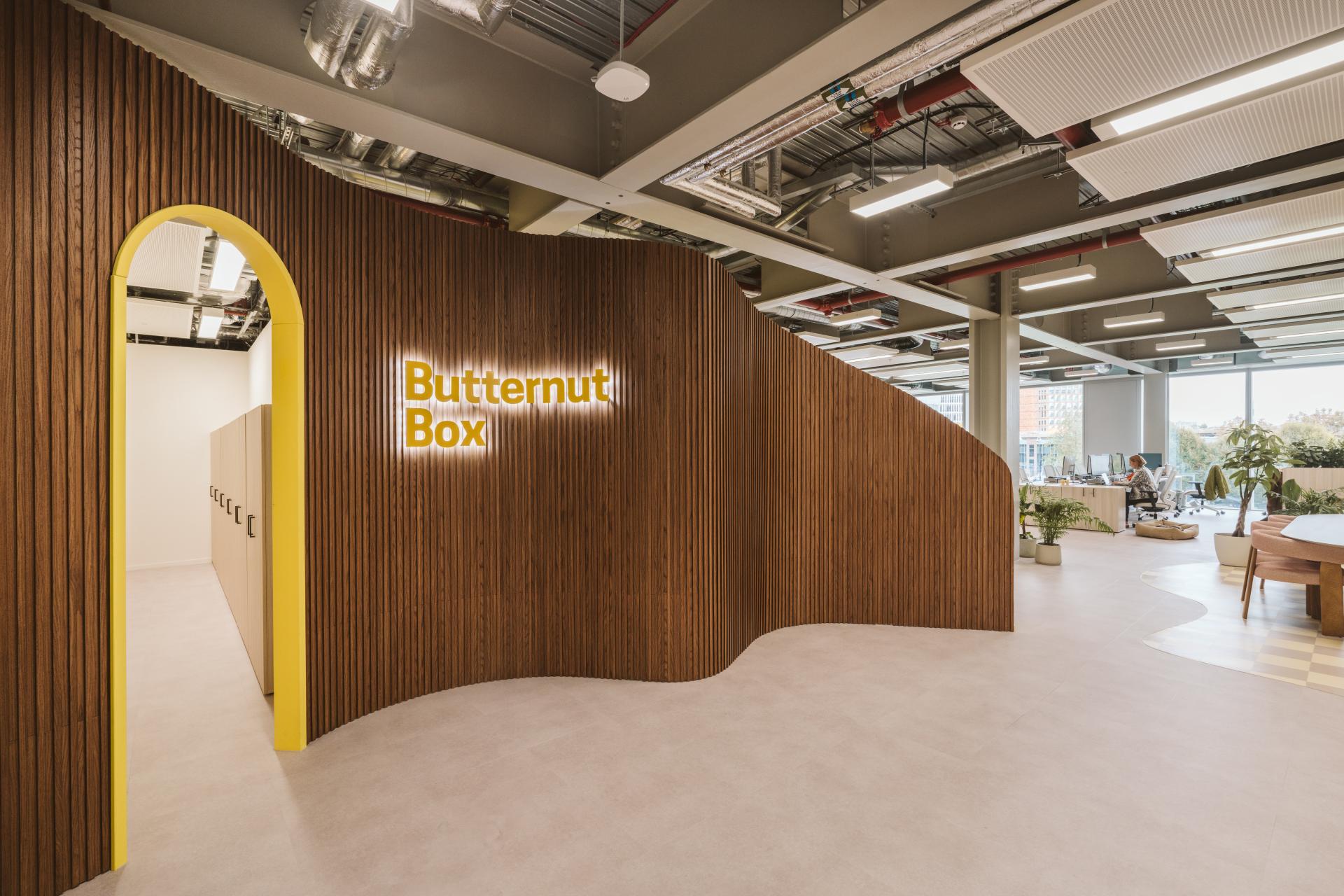 Modern office space of Butternut Box featuring wood paneling, bright signage, and an open layout designed for humans and dogs.