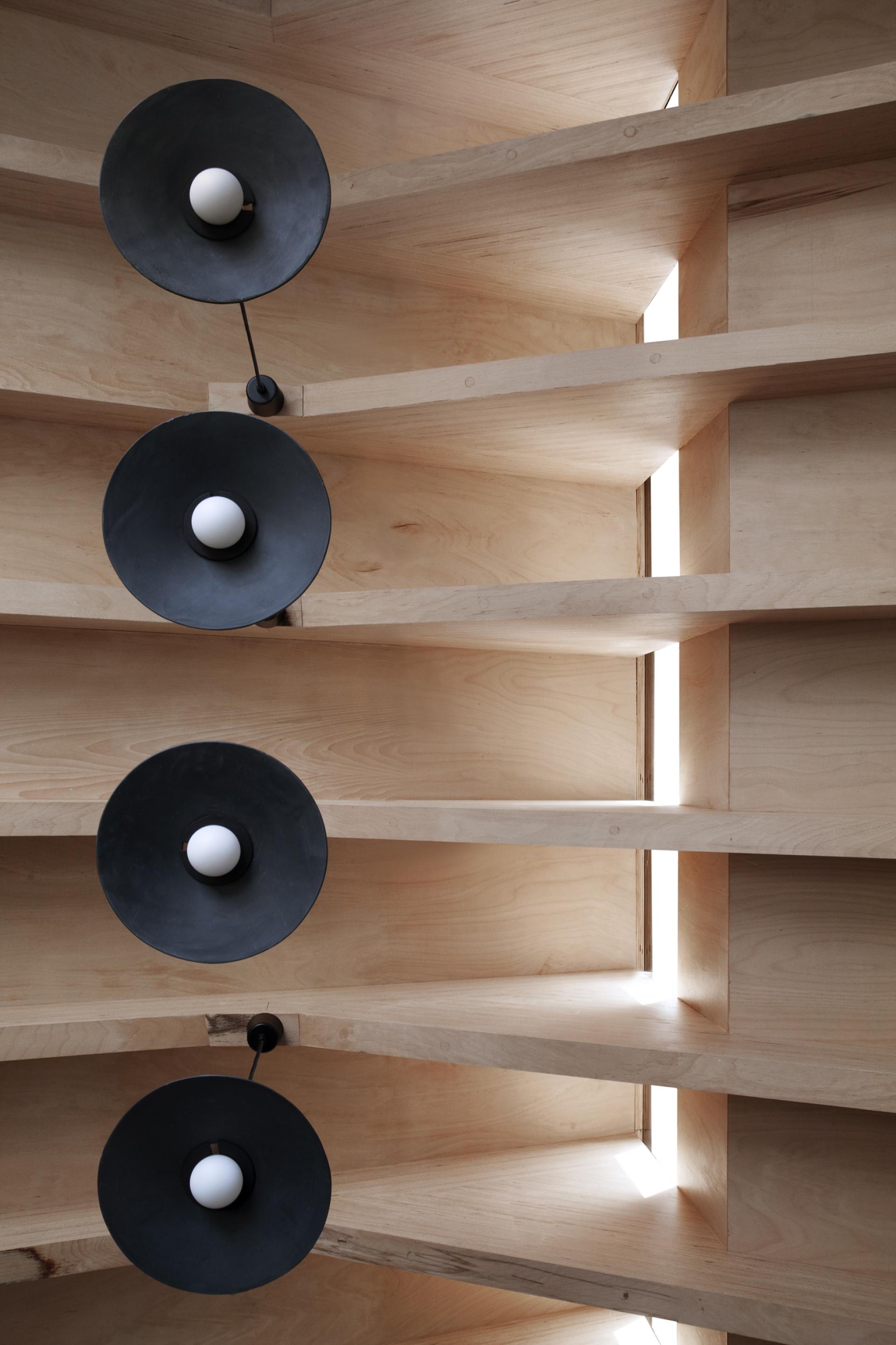 Stylish black lamps hang from a wooden ceiling, highlighting the innovative design elements of THISS architecture studio.