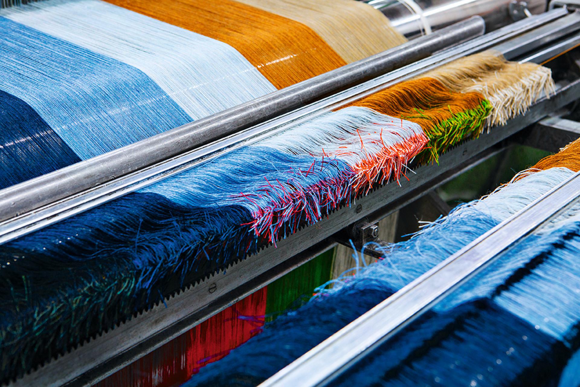 Vibrant threads in various shades of blue, orange, and green displayed on a textile weaving machine at Kvadrat.