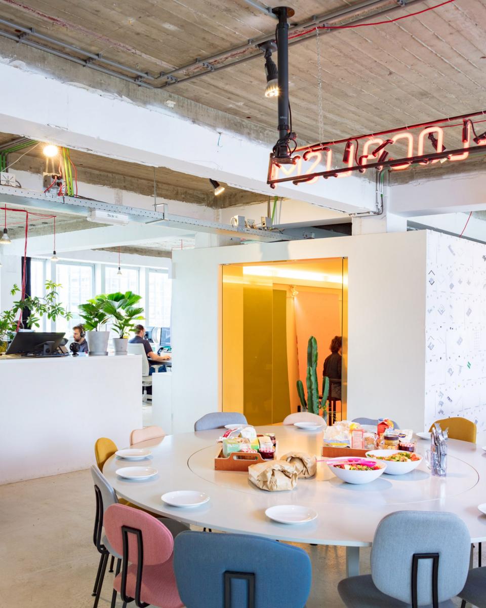 Bright, open architecture studio featuring a communal dining table with food, plants, and modern design elements.