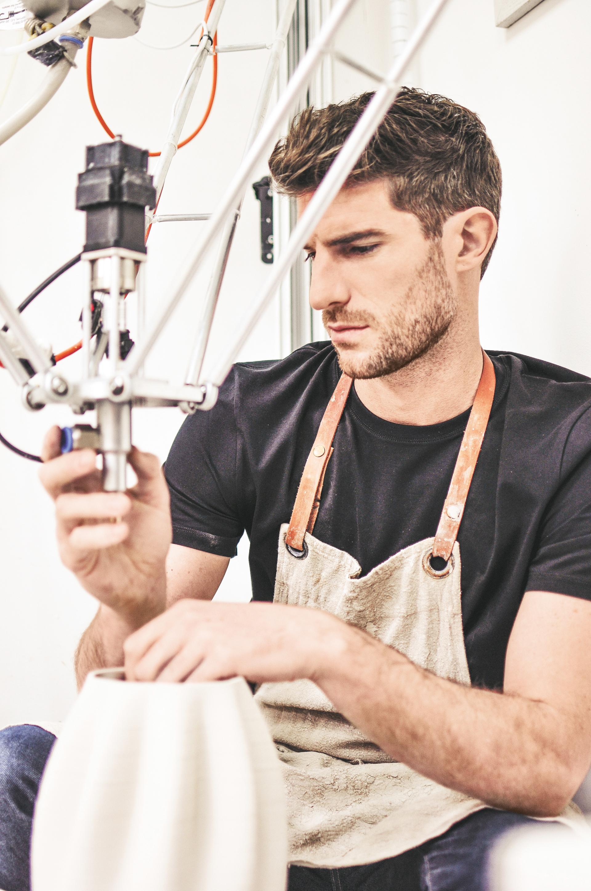 Ryan Barrett carefully crafts a ceramic piece using a 3D printer, showcasing innovation in modern pottery techniques.