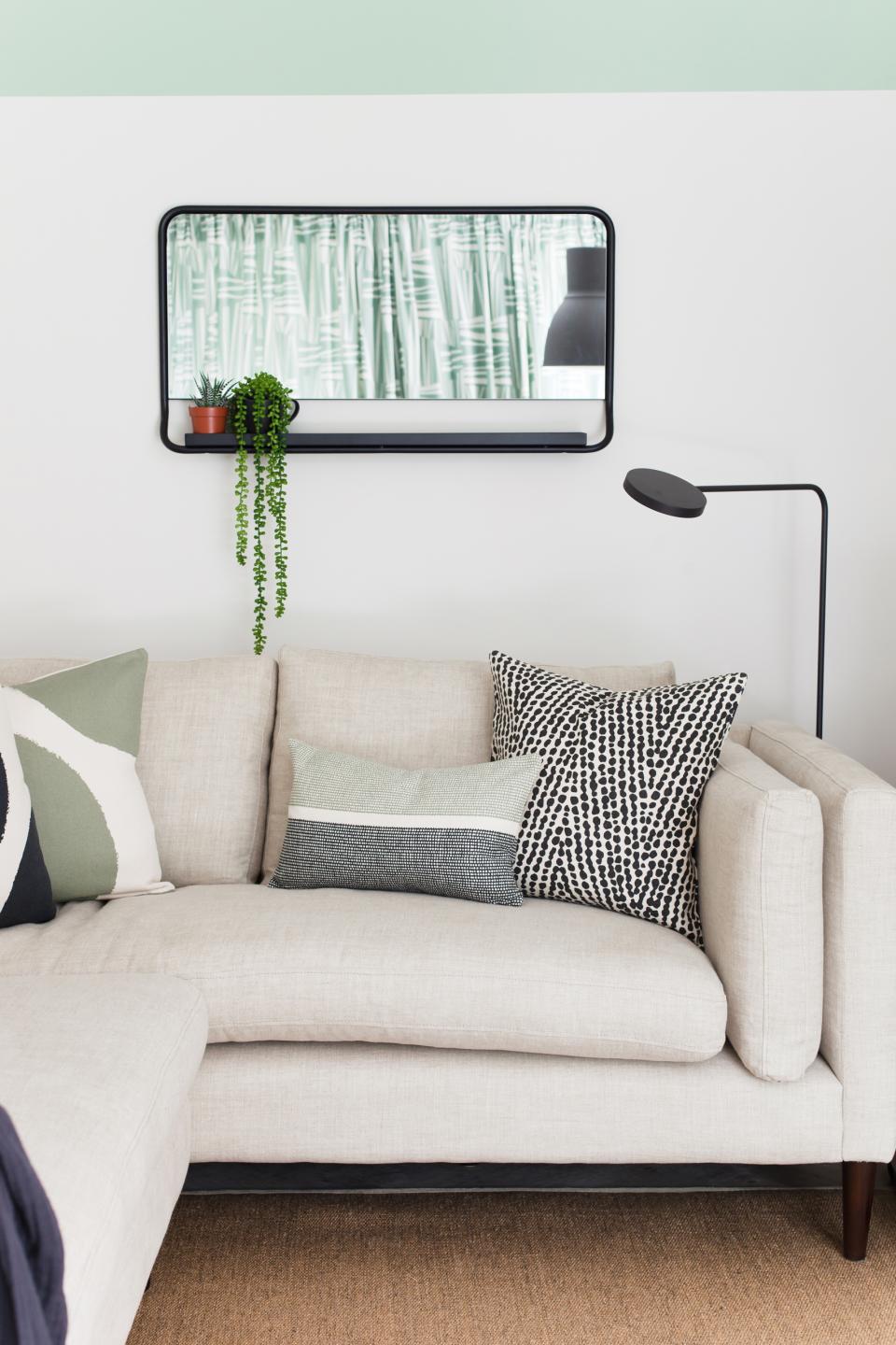 Stylish Scandi Industrial living room featuring a beige sofa, decorative pillows, and a minimalist wall mirror with plants.