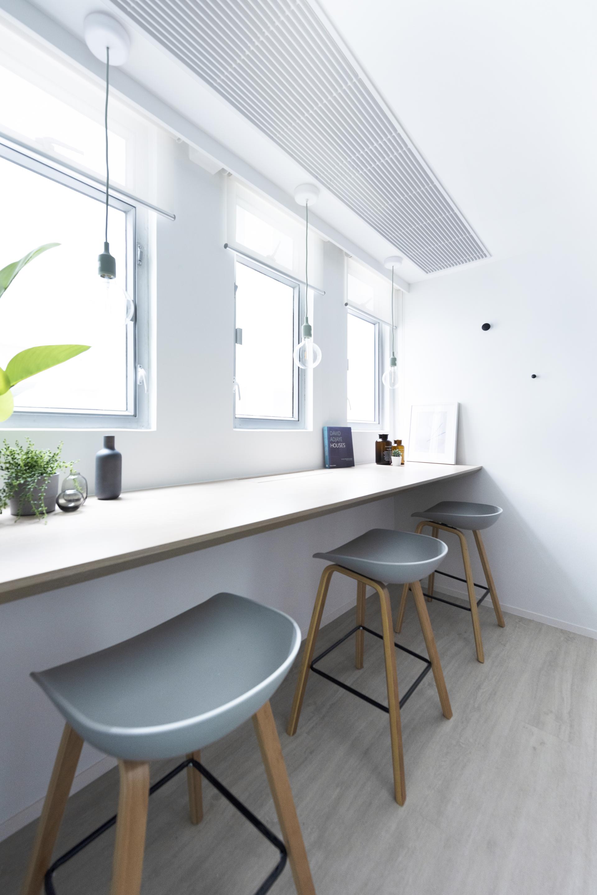 Contemporary workspace featuring minimalist design with gray stools, pendant lights, and natural elements, ideal for live-work environments.