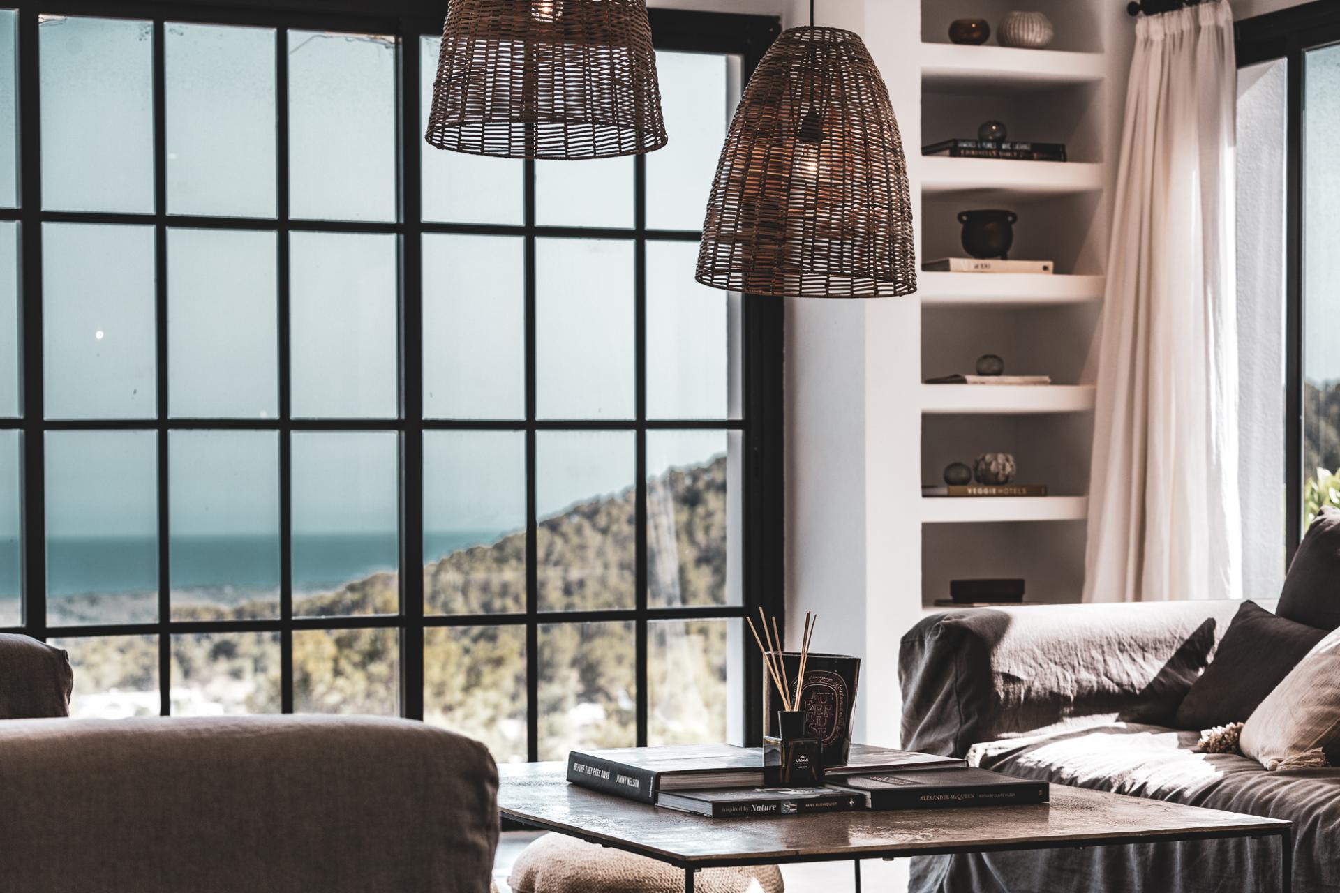 Stylish interior featuring a cozy seating area, woven pendant lights, and panoramic views of nature outside.