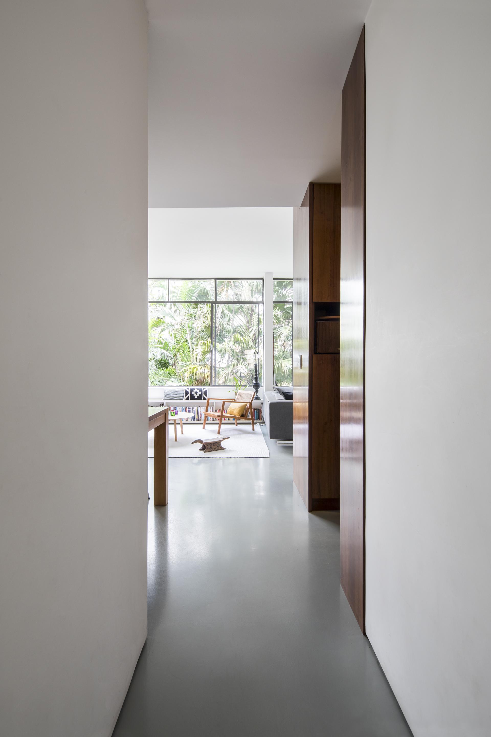 Renovated mid-century apartment hallway in São Paulo, featuring natural light and views of tropical gardens.