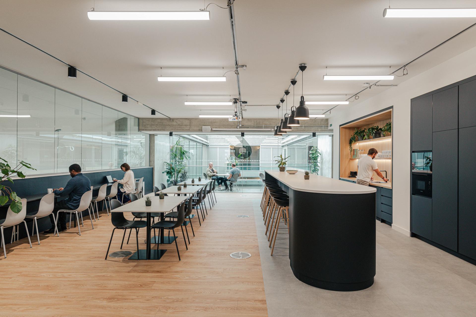 Modern open workspace for Lacoste, featuring a collaborative area, stylish bar seating, and a relaxed atmosphere with greenery.