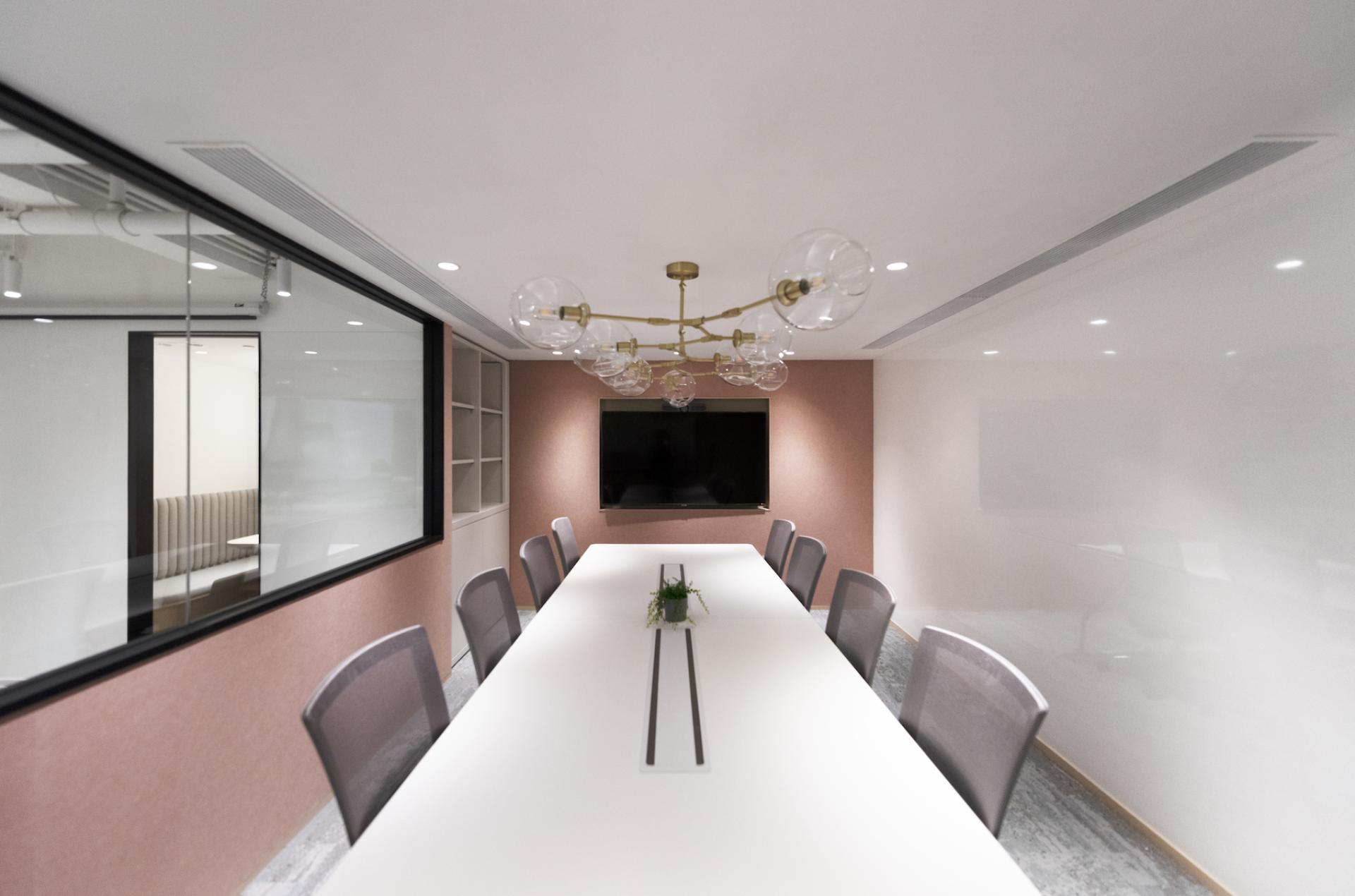 Modern conference room design featuring a long white table, stylish lighting, and a wall-mounted screen, ideal for collaboration.