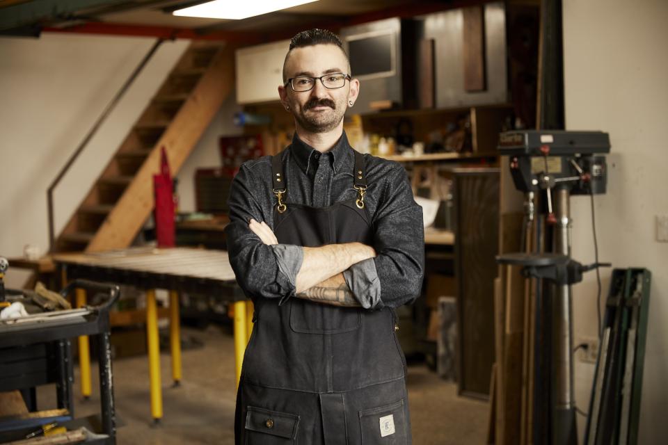 Brooklyn-based maker stands confidently in his workshop, showcasing craftsmanship and creativity in design.