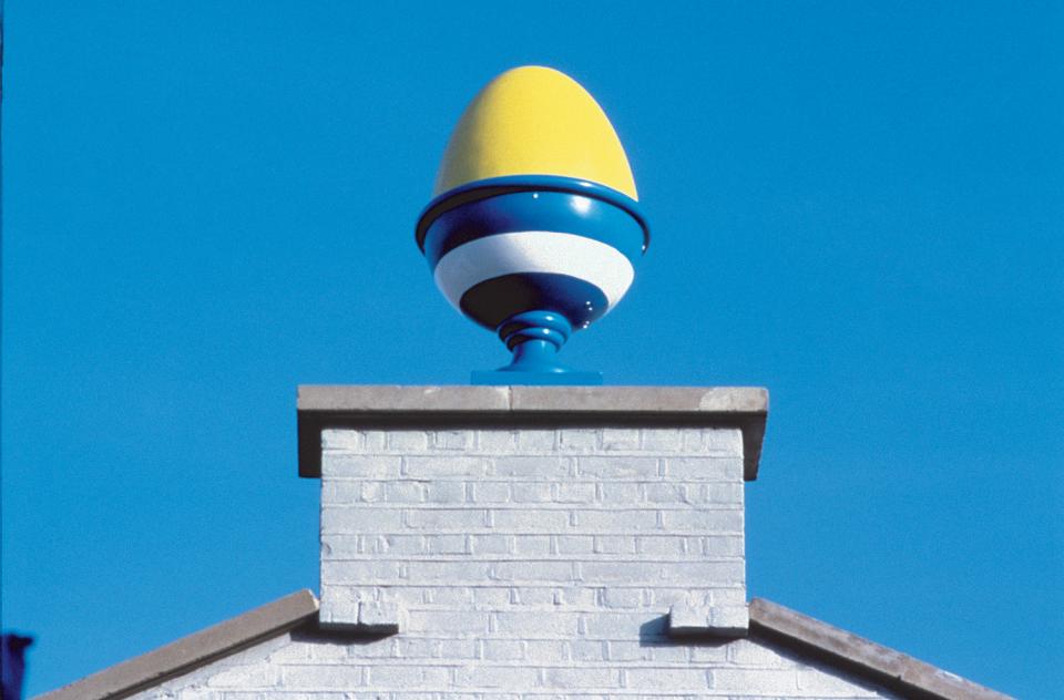 Colorful architectural feature resembling an oversized ornament atop a brick chimney against a clear blue sky.
