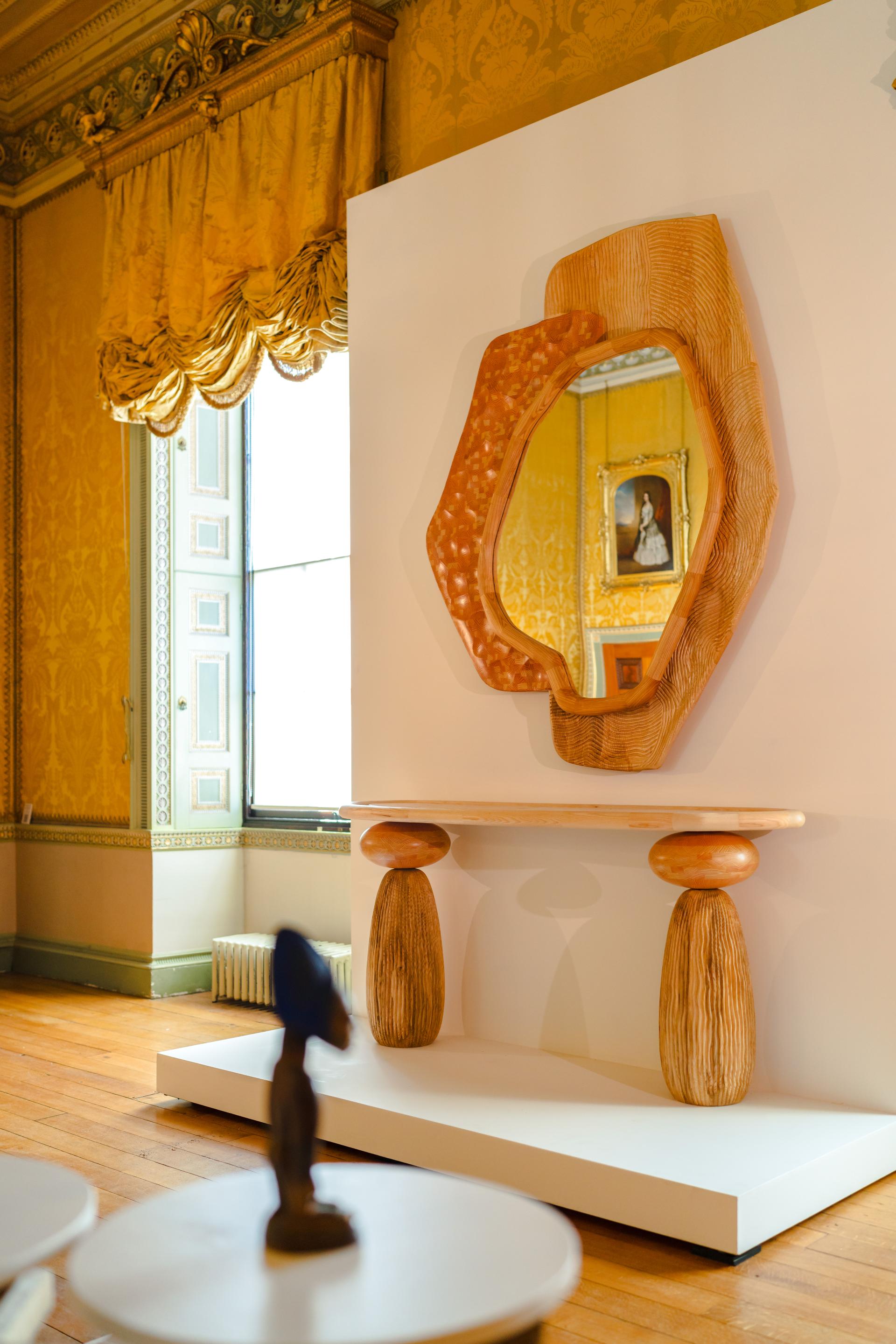 Stylish wooden console table with sculptural bases and a unique, textured mirror in an elegant interior setting.