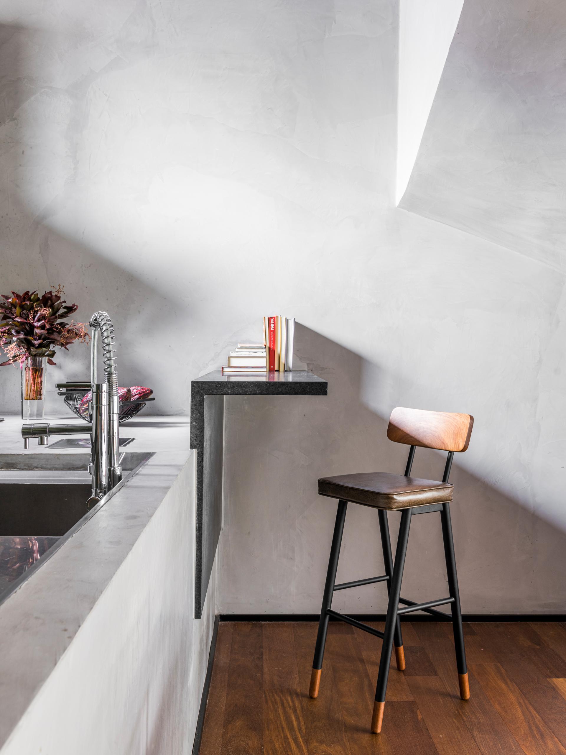 Modern kitchen corner featuring a sleek countertop, stylish stool, and decorative books, highlighting contemporary design elements.