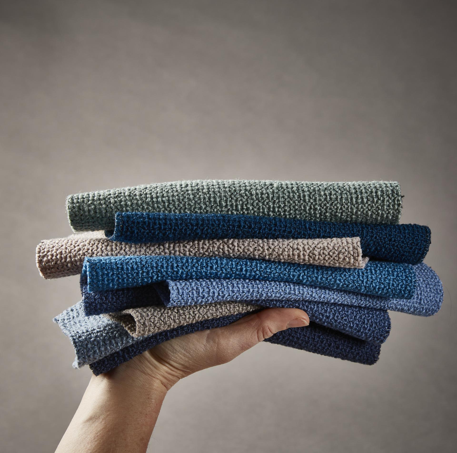 New spring colors of Camira's Yoredale bouclé fabric displayed in a hand, showcasing a variety of textured wool options.
