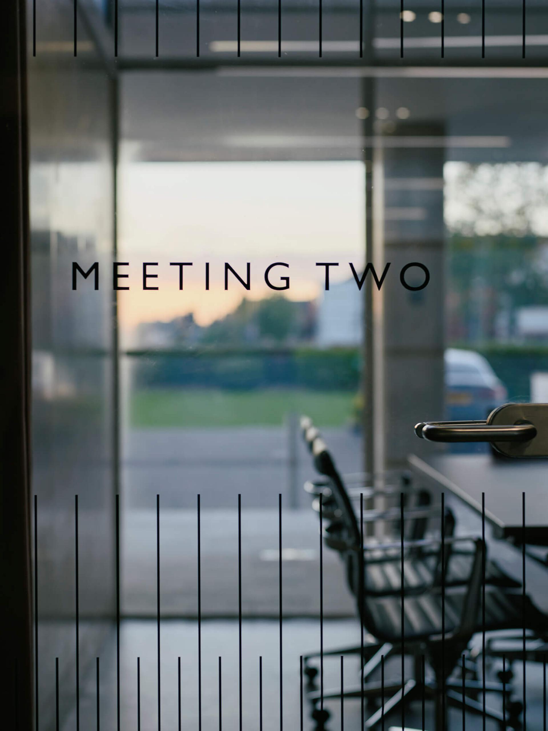 Modern glass door labeled 'Meeting Two' with stylish conference room chairs and a view of the outdoor landscape.