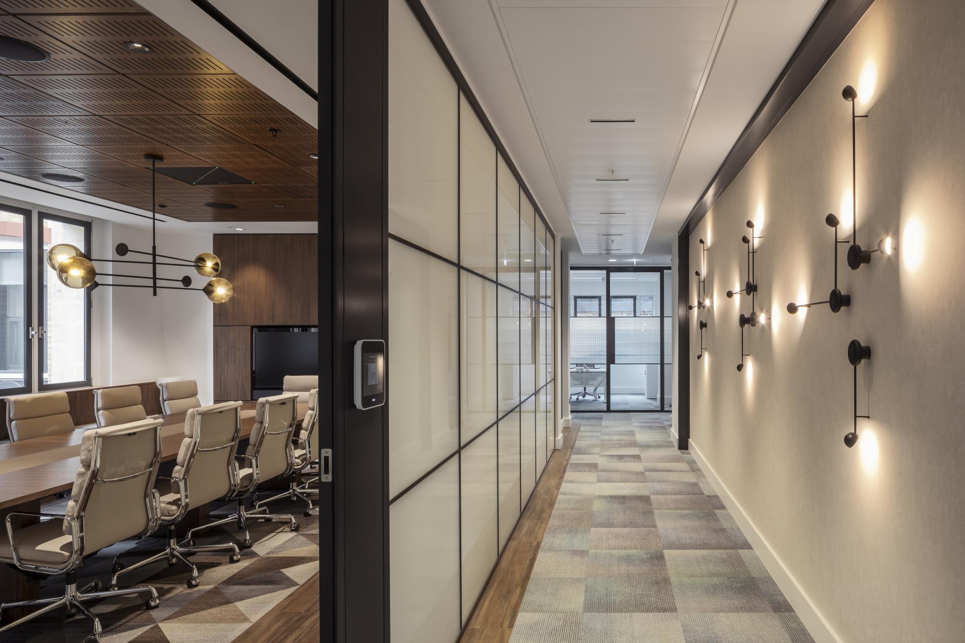 Modern office hallway with glass partitions, stylish lighting, and a conference room showcasing contemporary design elements.
