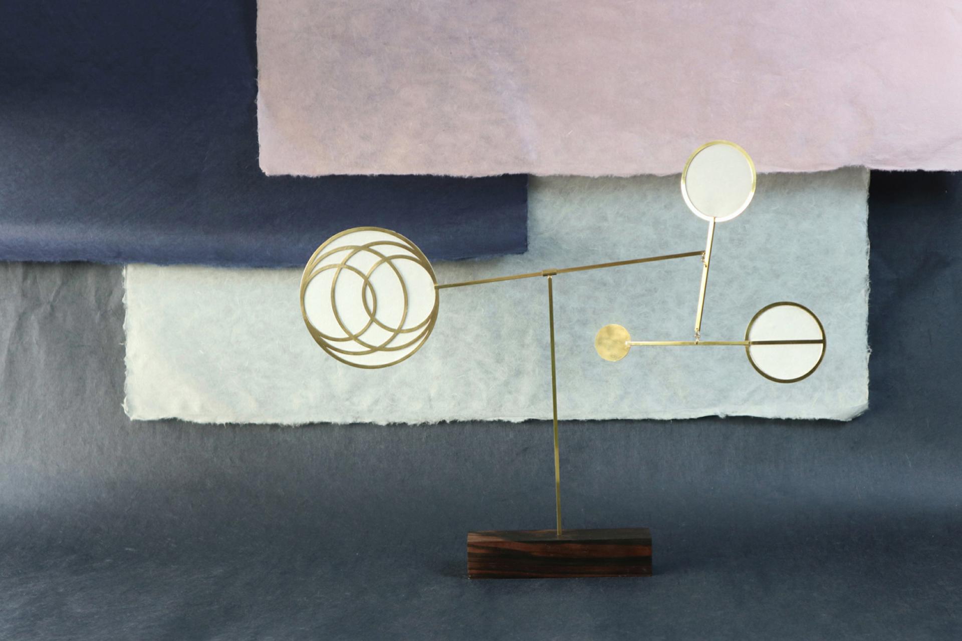 Artistic brass sculpture with circular accents displayed against layered pastel backgrounds at designjunction event in London.