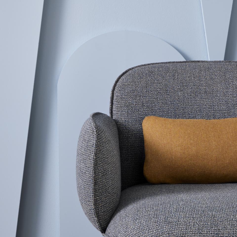 Stylish gray armchair upholstered in Camira Main Line Twist tweed, featuring a mustard-colored accent pillow against a soft background.