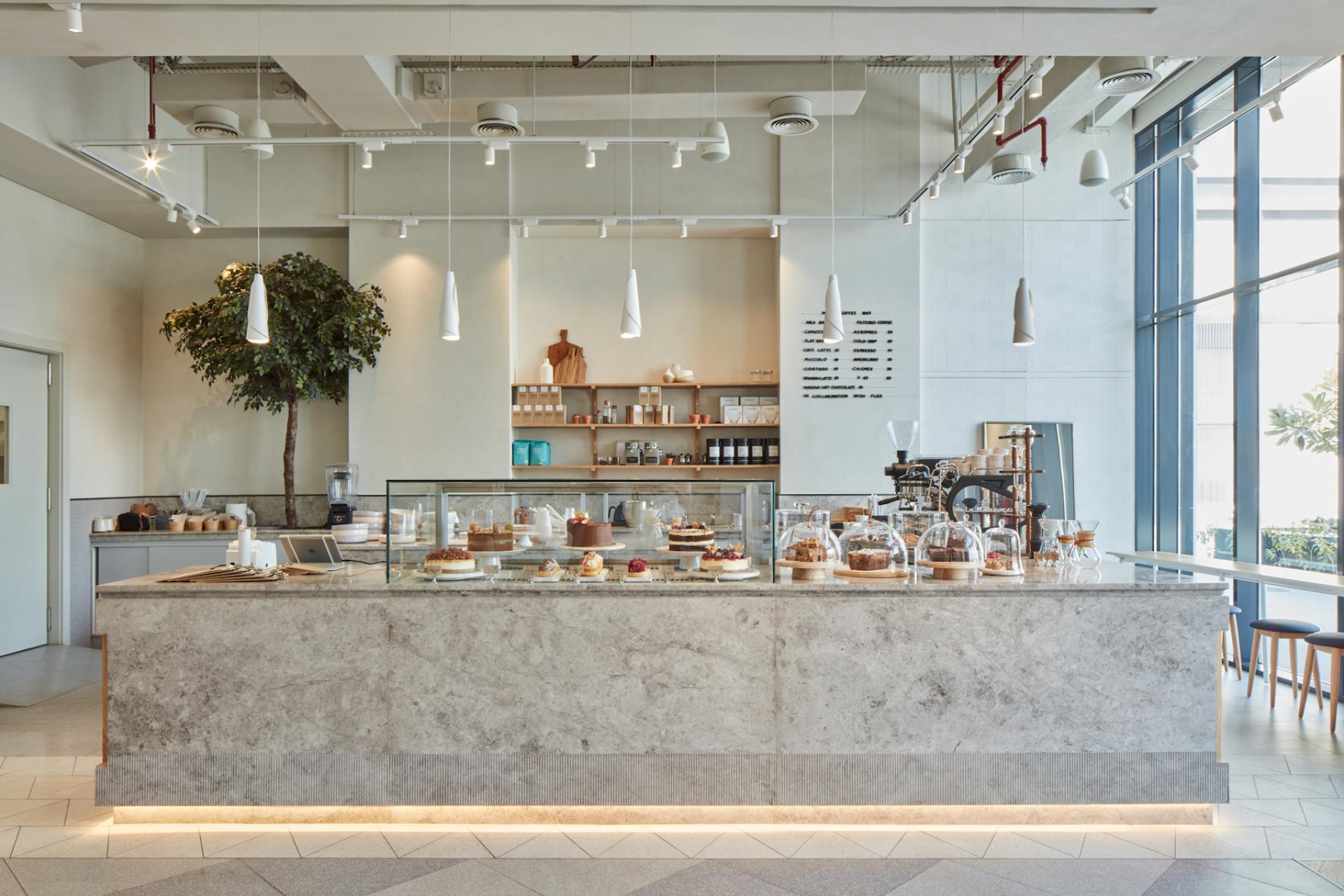 Modern café interior featuring a marble counter with pastries, greenery, and a contemporary design in Dubai.