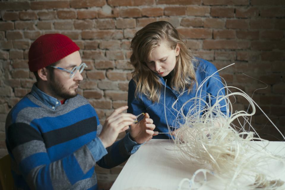 Two designers examine a biodegradable natural plastic material in a creative workspace, exploring innovative applications for Nuatan.