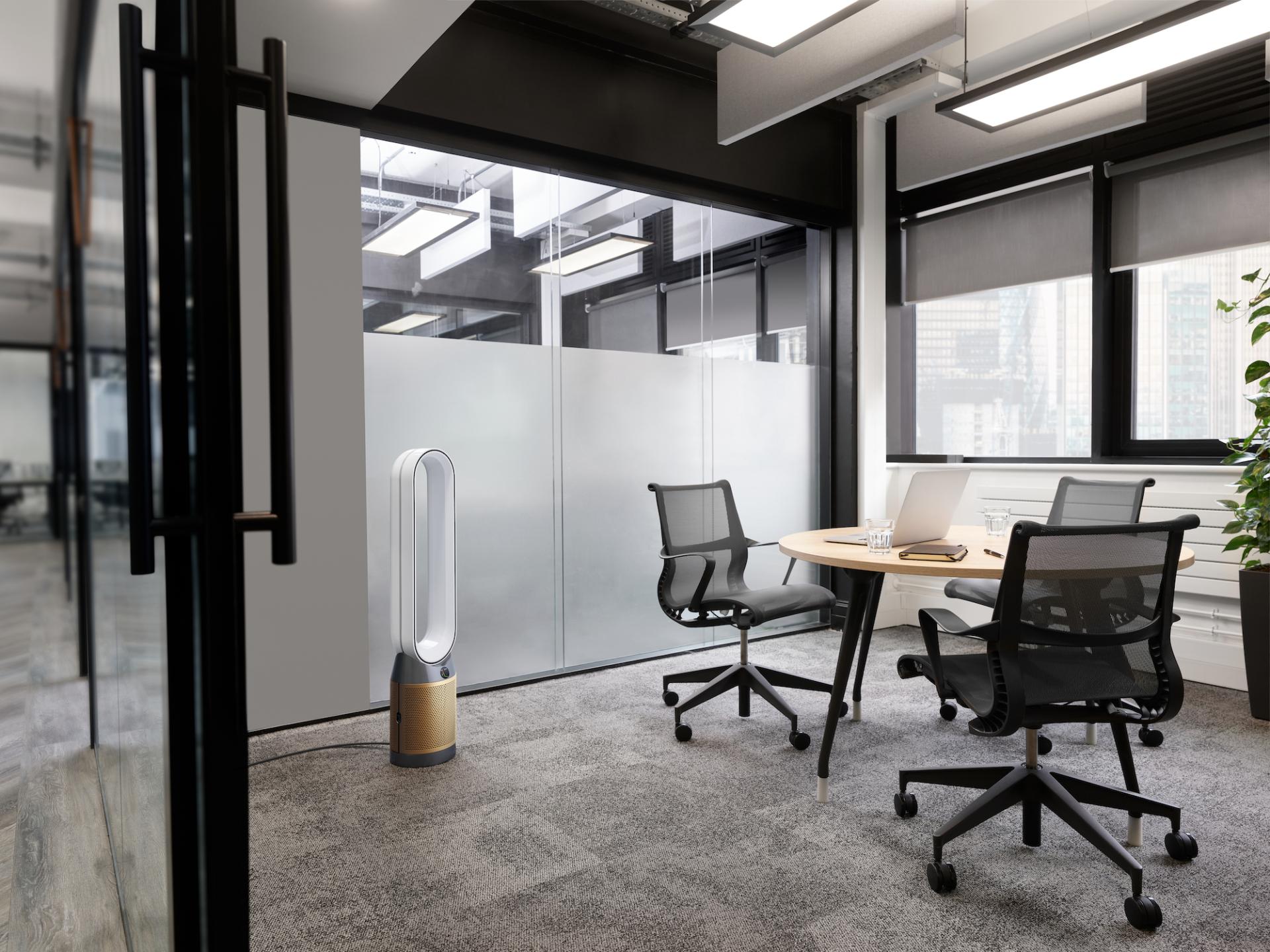 Modern office space featuring a sleek Dyson air purifier, wooden table, and ergonomic chairs, showcasing innovative design in Manchester.