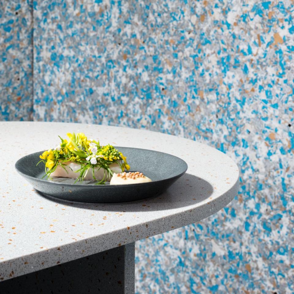 Delicately arranged dish featuring vibrant flowers and vegetables on a stylish plate, set against a textured blue background.