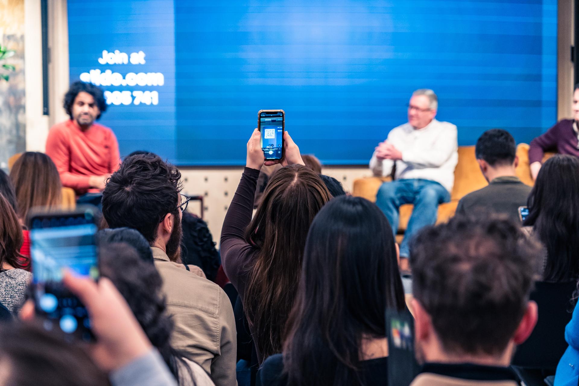 Audience engaged in a discussion about achieving Net Zero, with a speaker visible in the background.