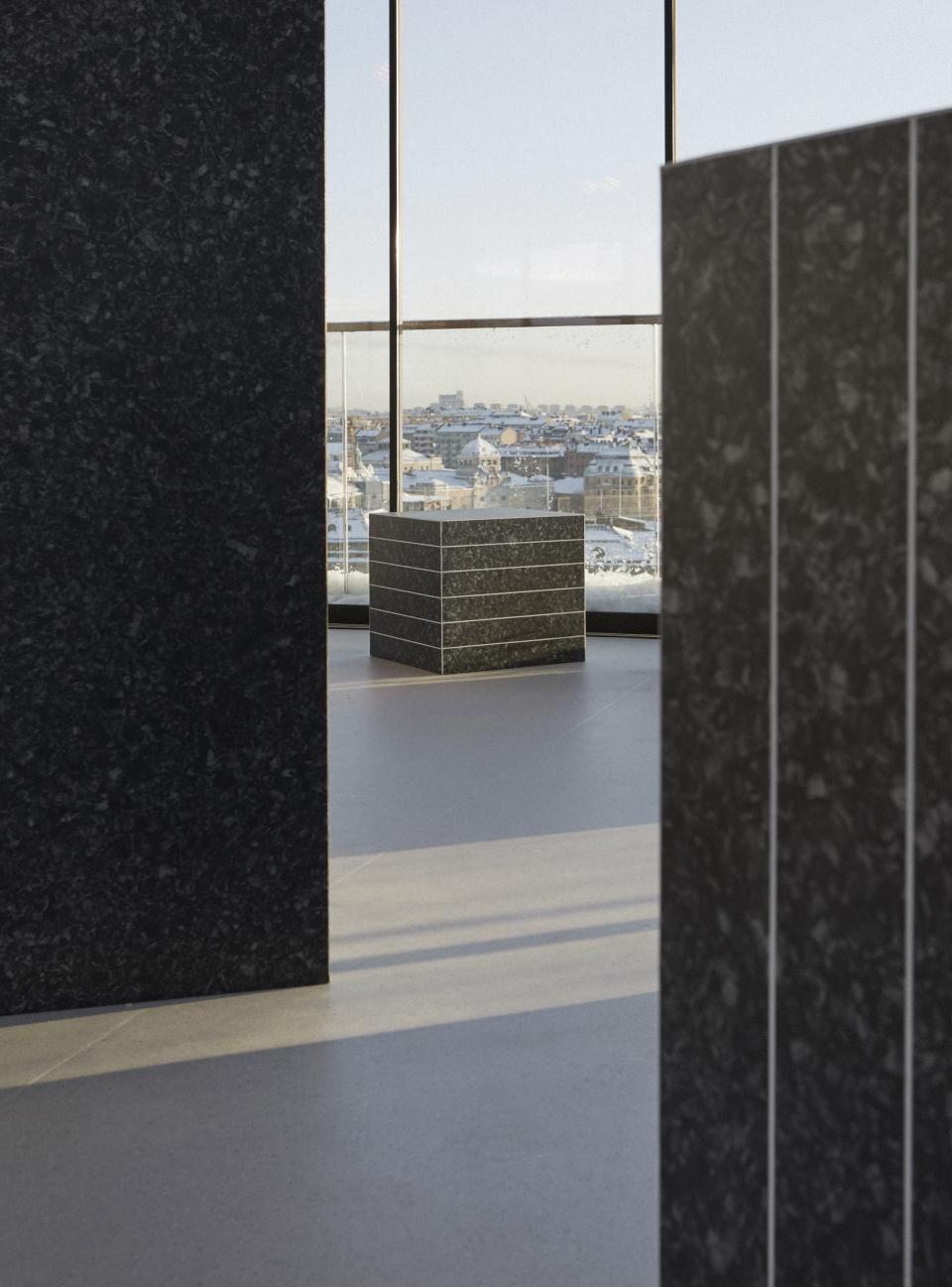 Modern exhibition space featuring sleek, dark sculptural elements with a panoramic winter city view of Stockholm outside.