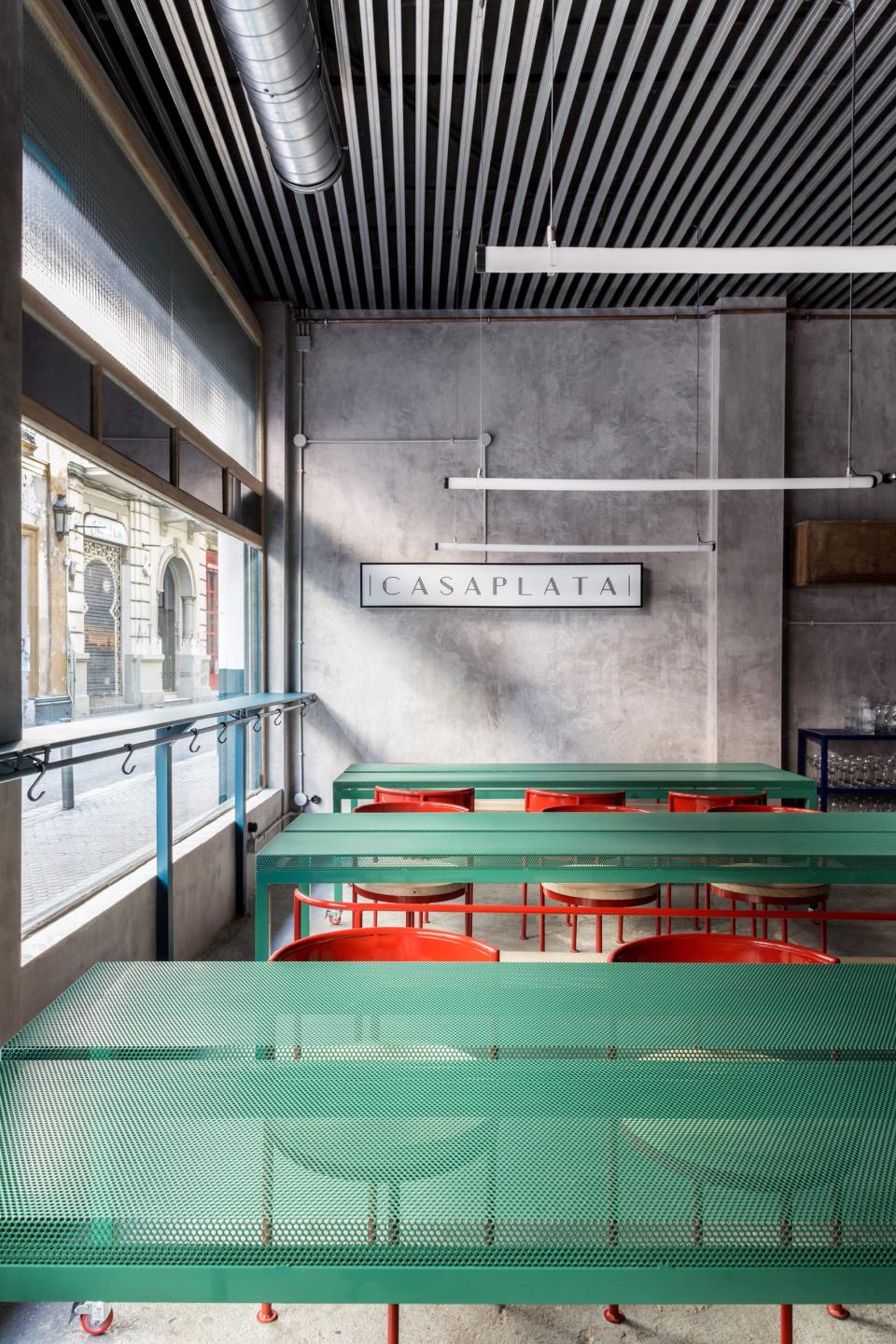 Modern restaurant interior featuring concrete walls, green mesh tables, and vibrant red chairs in Seville.